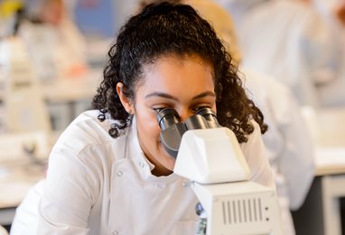 Researcher in a white coat looking into a microscope