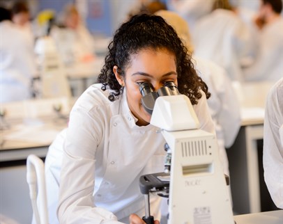 Biomedical student in white lab coat looking into a microscope