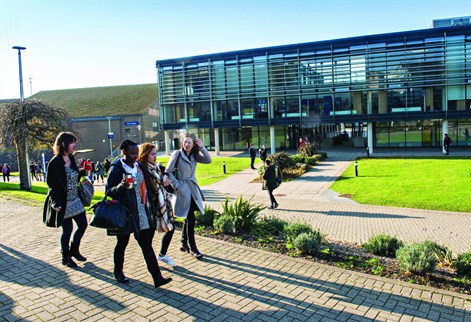 Four students walking past the Checkland Building at Falmer