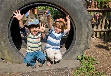 Two children at nursery playing in tire swing