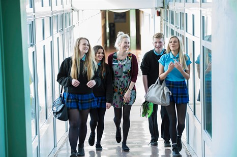 Group of pupils and fealle trainee teacher walking along a corridoor in school