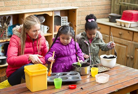 female teacher and two girls playing in mud kitchen