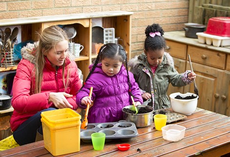 Female teacher and children playing in a mud kitchen