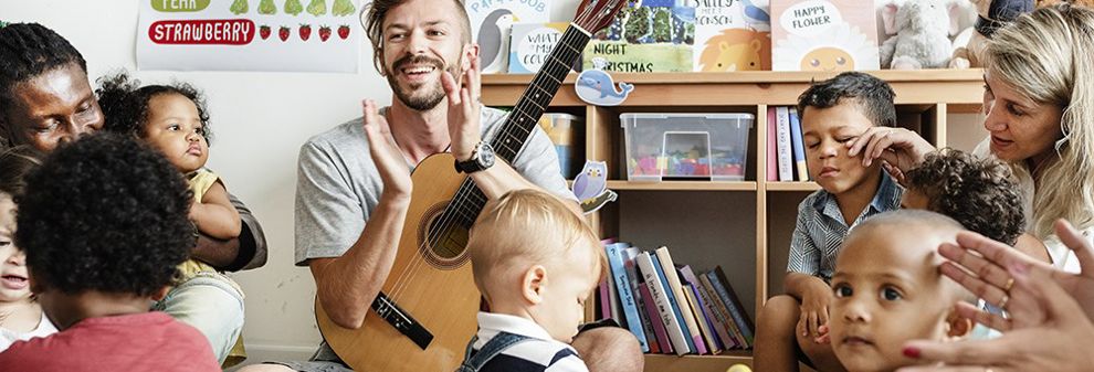 Male teacher playing guitar to a group of toddlers