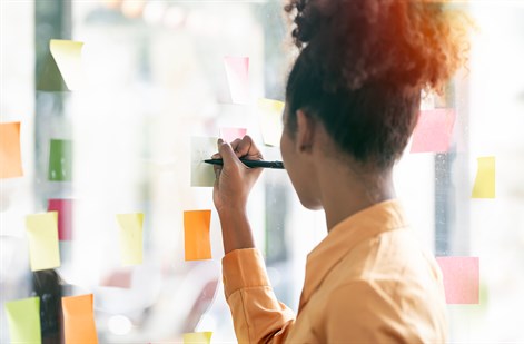 female student writing on post it note on wall