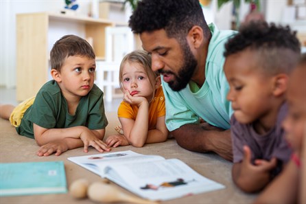 male teacher reading book with group of toddlers