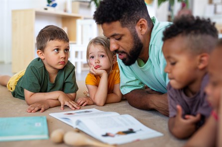 male teacher reading book with group of toddlers