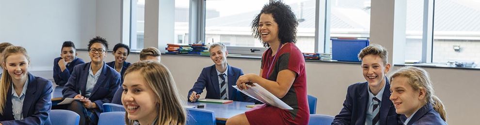 teacher sitting on desk with students