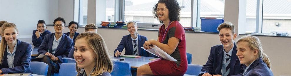teacher sitting on desk with students