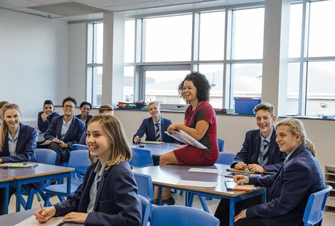 teacher sitting on desk with students