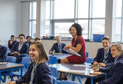 teacher sitting on desk with students