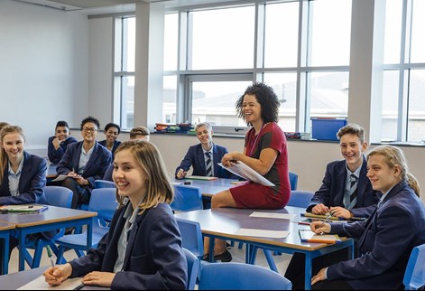 teacher sitting on desk with students