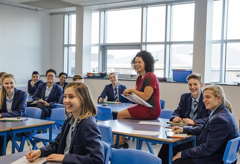 teacher sitting on desk with students