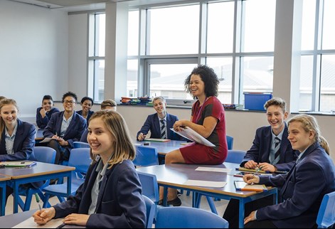 teacher sitting on desk with students