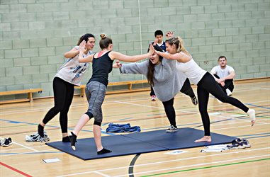 Four students balancing around the outside of an exercise mat