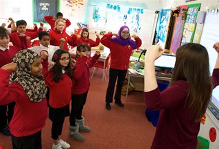 Group of primary children in classroom with arms up