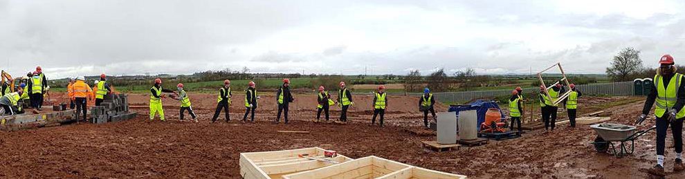 A line of construction students in a muddy field wearing hi-viz