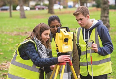 Two female and one male student wearing high vis jackets using survey equipment