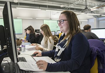 Female student smiling looking at computer screen with two female students in the background