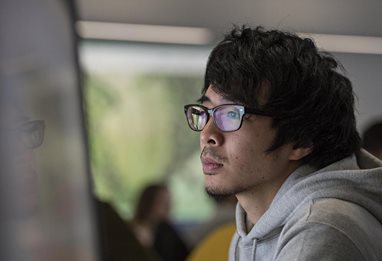Male student wearing glasses looking at computer screen