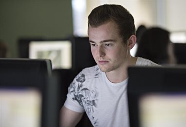 Male student surrounded by computer screens