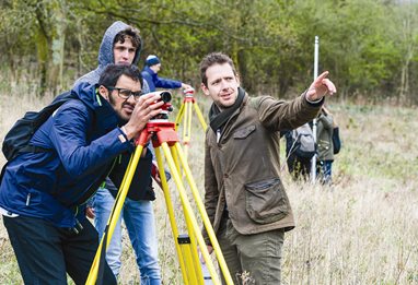 Two students and a lecturer using field surveying equipment in a field