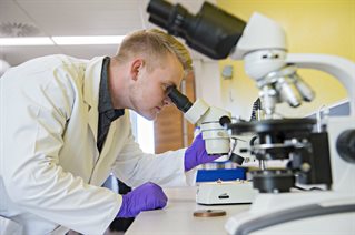 Student in a lab coat looking in a microscope