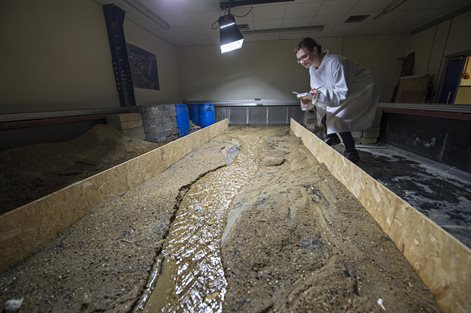 Lecturer standing beside simulated river bed in a room