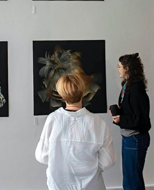 two people view an art installation, six square pictures hung in grid on a white wall