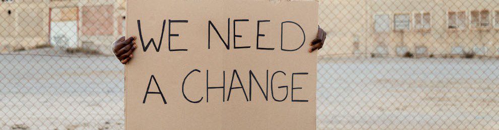 person holds handmade banner saying we need a change
