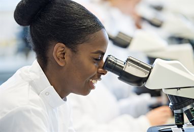 Smiling student looking down microscope