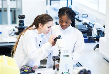 Two students working in the lab with a microscope