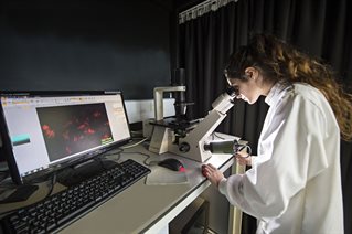 Researcher in lab coat with electron microscope attached to computer equipment