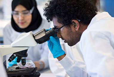 Close up of a student in a white coat looking into a microscope