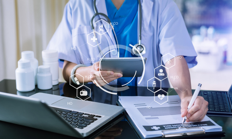 Pharmacist using a tablet and a notepad at a desk in a medical setting