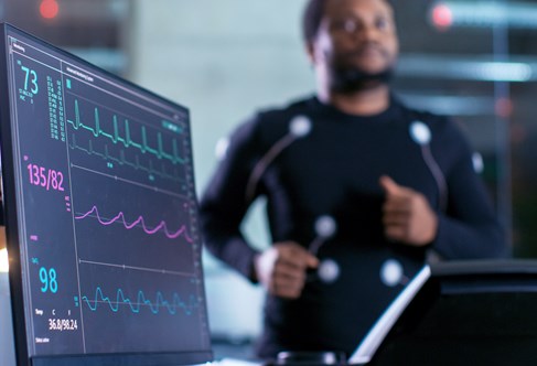 Athlete wearing high tech clothing with sensors on treadmill with computer display of heart rate