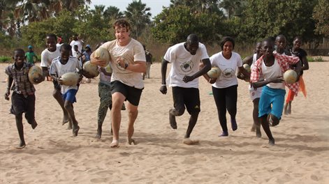 group running on the beach with a rugby ball