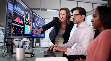 Three colleagues reviewing data dashboards on large monitors