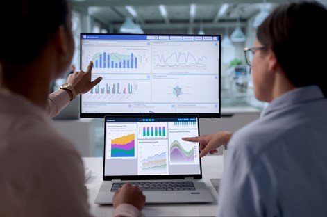 Two people reviewing charts and data dashboards on laptop and computer