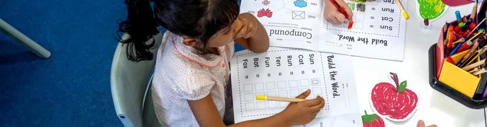 Primary children sat a a table working on colourful learning activity sheets
