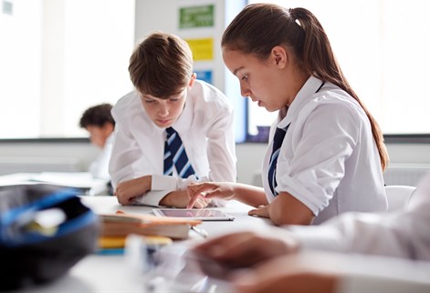Students students using a tablet device together during a classroom learning activity.