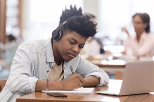teenager works on revision while listening to podcast on bluetooth headphones