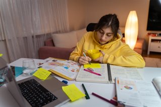 Student sits at desk revising for exams using post-it notes and a mind map