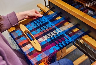 Close up of a student weaving at a loom