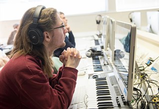 A student wearing headphones in front of a keyboard and computer