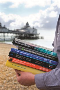 Hands carrying books, seafront in the background