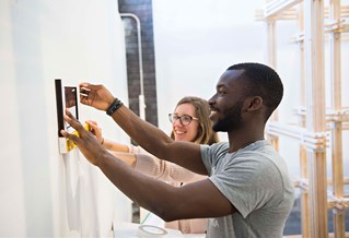 Two students fixing a framed piece of art to a wall