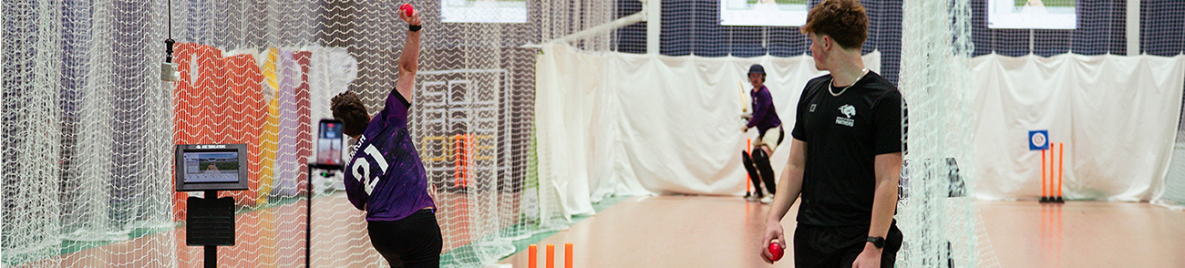 Three people playing cricket in indoor facilities