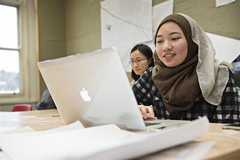 female student wearing hijab working on laptop in studio