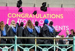 A group of graduates on the seafront promenade throwing their motor boards in the air